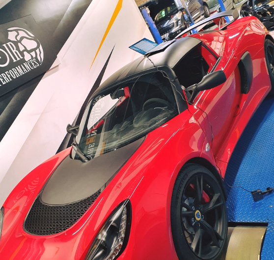 Voiture de sport Lotus rouge, toit et capot noirs, sur une surface bleue dans un magasin.