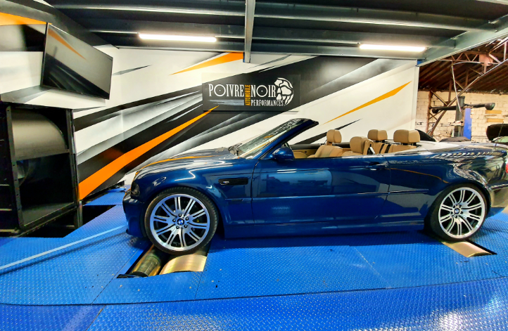 Cabriolet BMW bleu sur un dynamomètre bleu dans un magasin, avec des accents orange, noirs et blancs.