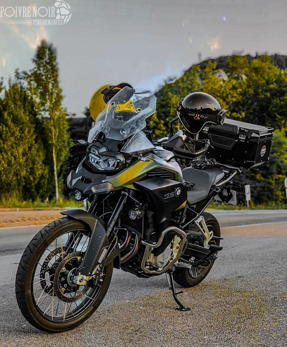 Moto BMW noire garée sur le bord d'une route avec casques et bagages, arbres en arrière-plan.