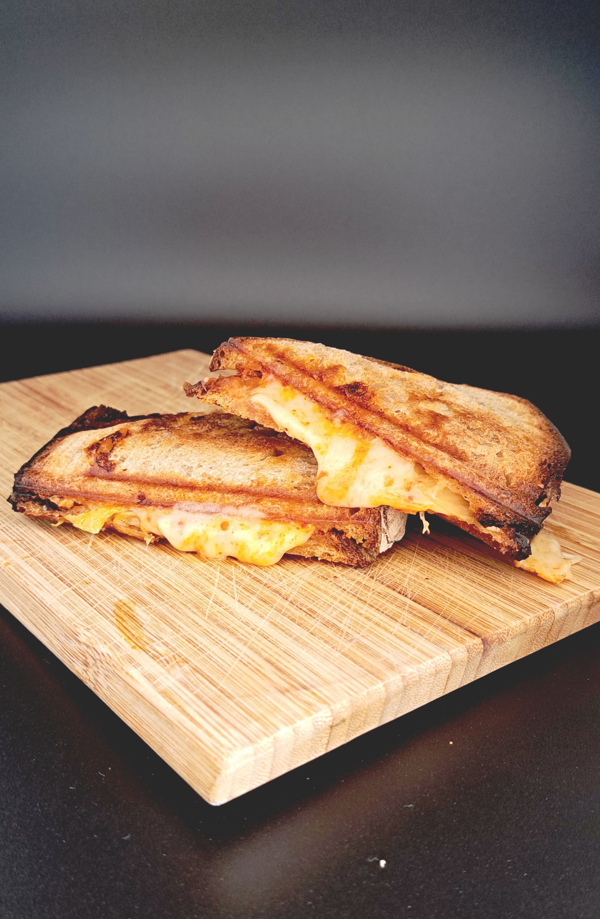 Un sandwich au fromage grillé est coupé en deux sur une planche à découper en bois