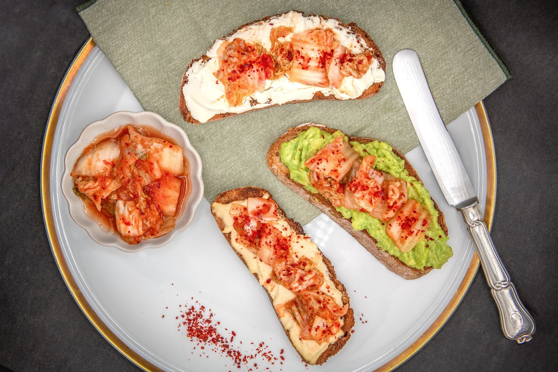 Toast au kimchi sur une assiette avec un bol de kimchi et un couteau, vue de dessus.