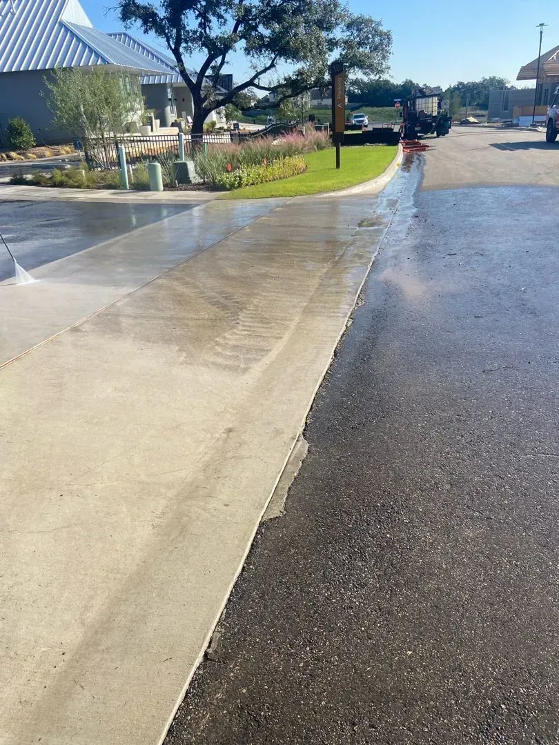 Concrete walkway split, one side wet, one side dry. Landscaping in background.