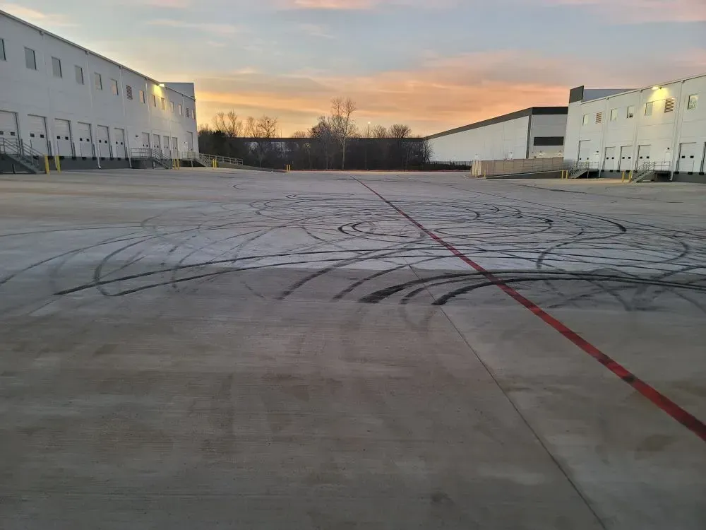Concrete lot with tire tracks between two white industrial buildings at sunset.