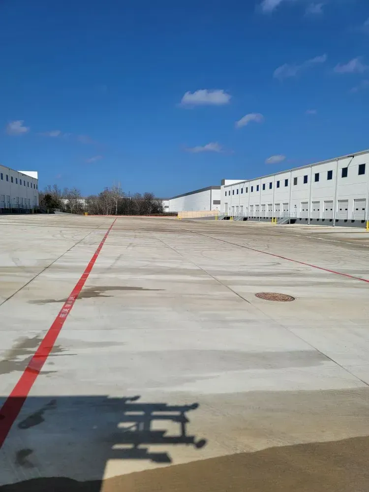 Large, empty concrete lot with loading docks and a blue sky.