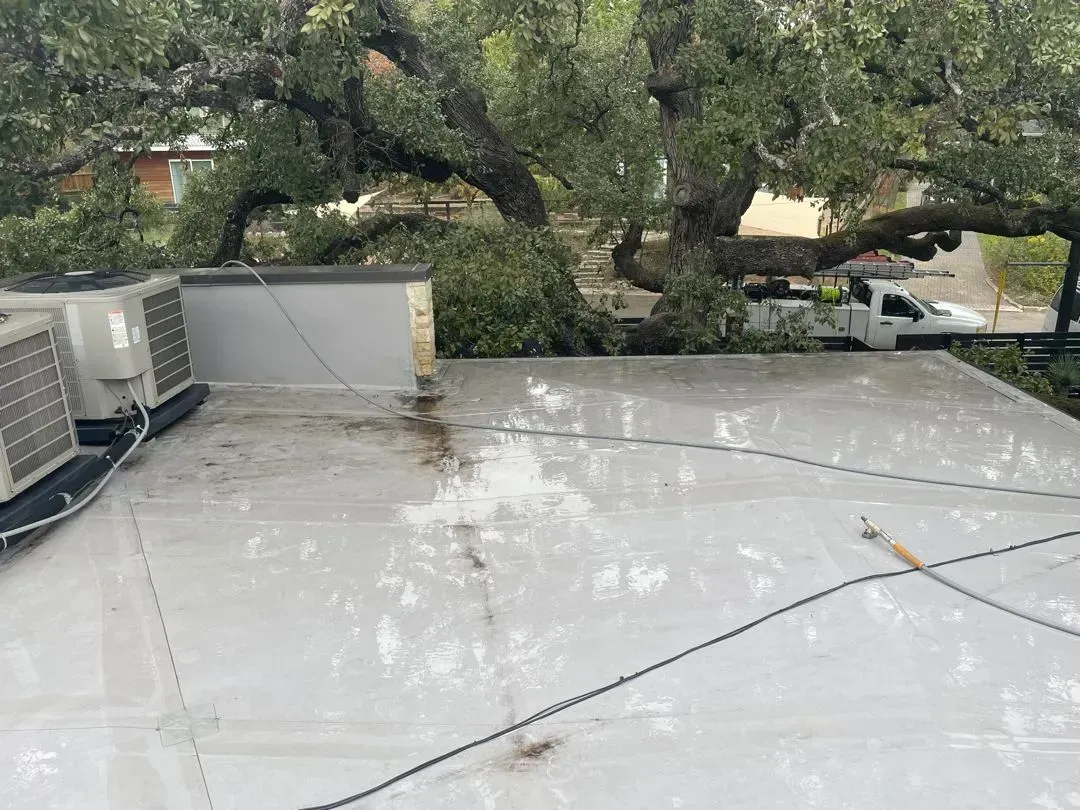 Flat rooftop with AC units, wet surface, and a large tree in the background. A white truck is visible.