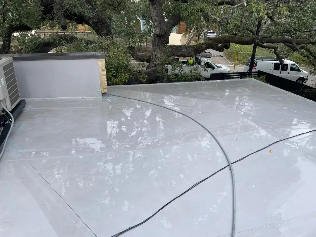 White, flat roof with reflection of a tree, an air conditioner, and black cables.