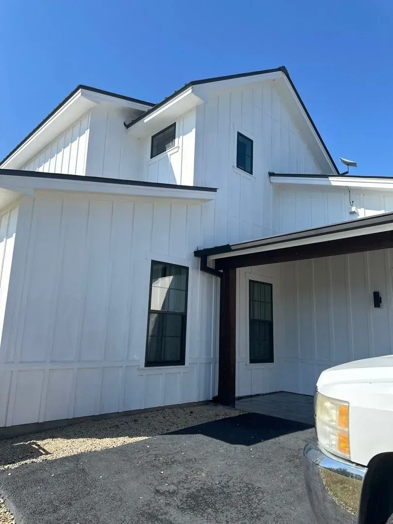 White house with dark trim and windows; blue sky.