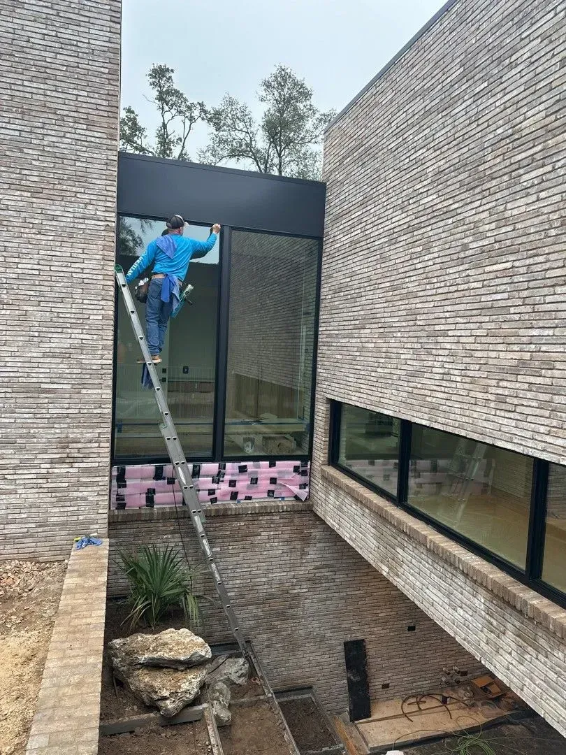 Man on ladder cleaning a large window of a brick building.