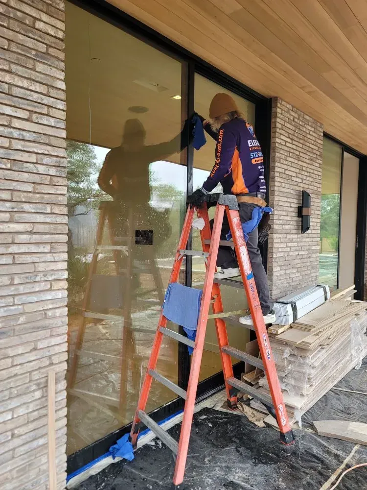 Person on a ladder cleaning a large window of a modern brick building.