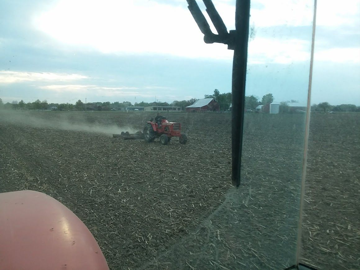 A tractor is plowing a field with a barn in the background