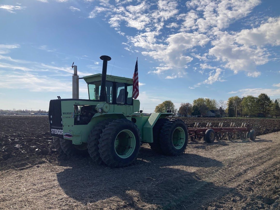 A green tractor is parked in a dirt field.