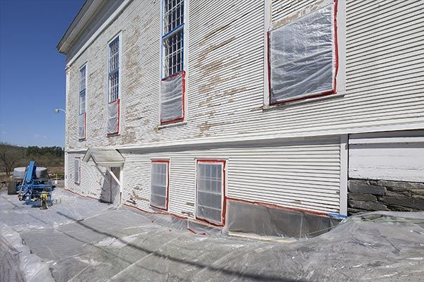A white building with plastic covering the Lead Paint windows is being painted.