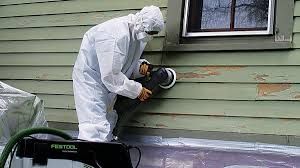 A man in a protective Lead paint suit in RI is sanding the side of a house.