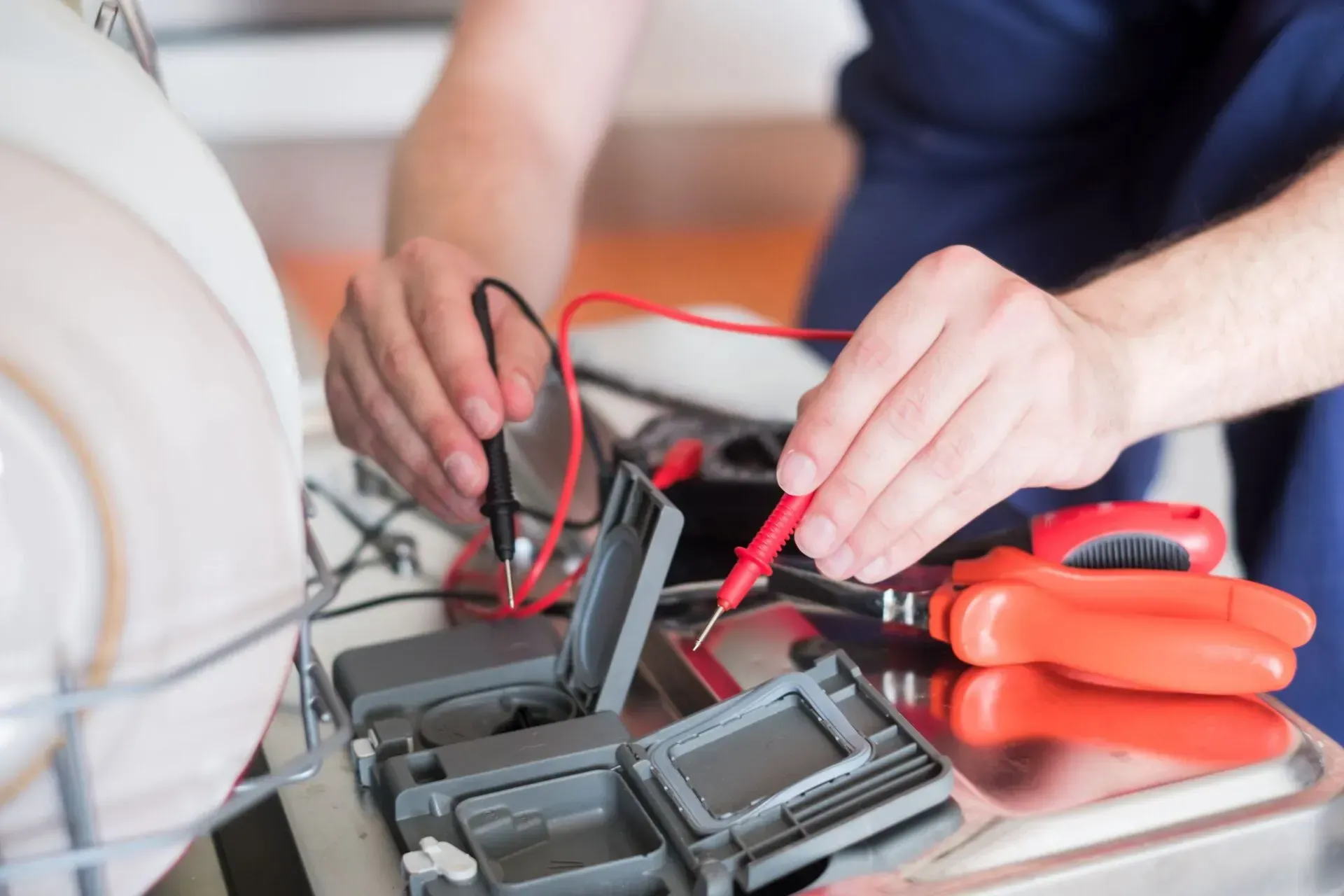 A man is fixing a dishwasher with a multimeter.