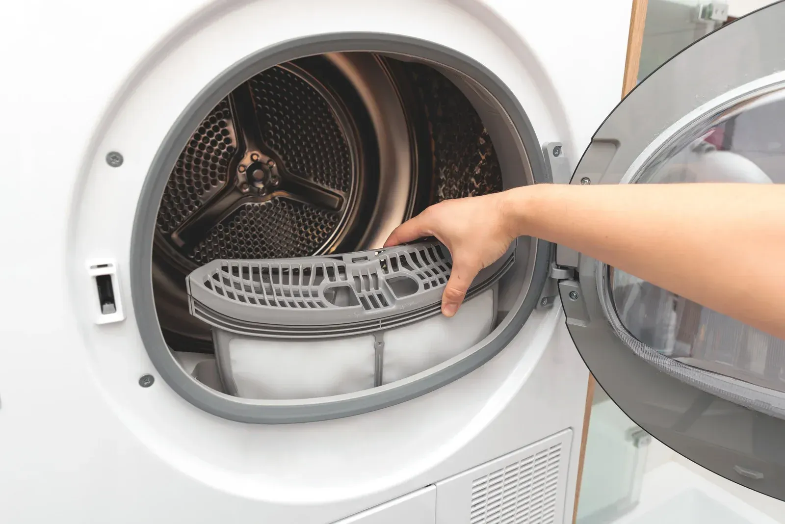 Hand removing lint trap from a white dryer.