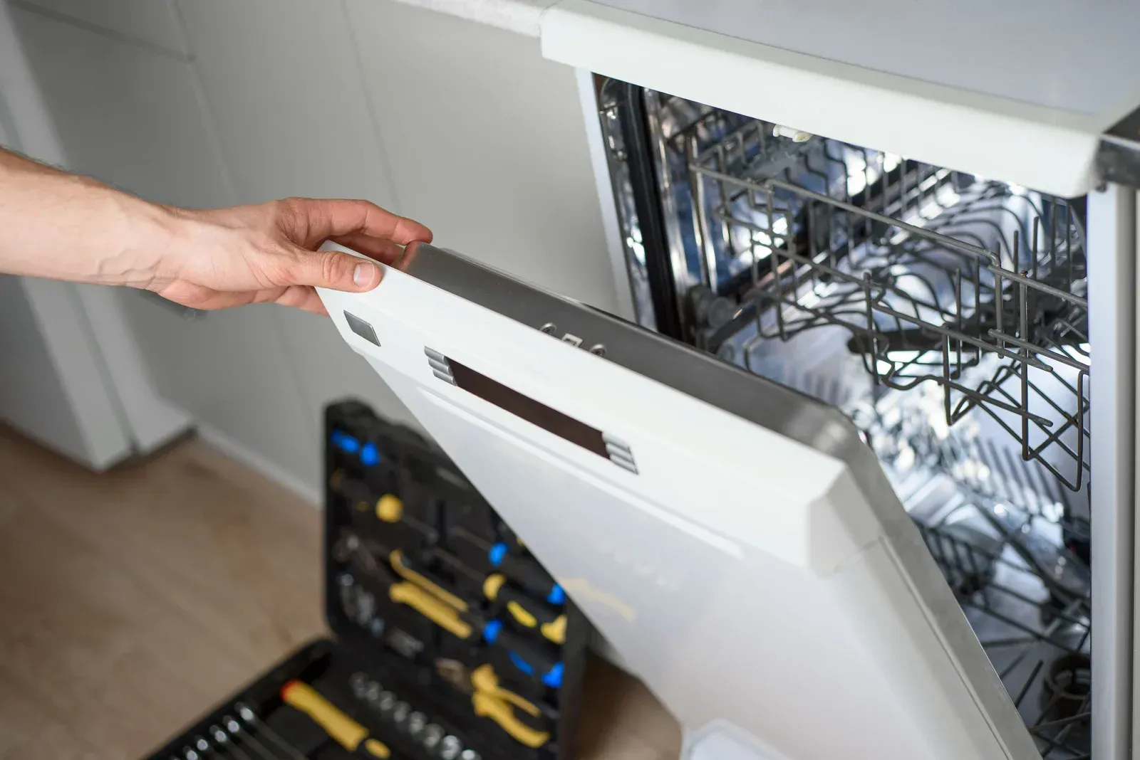 Person opening a dishwasher door with a toolbox in front of it.