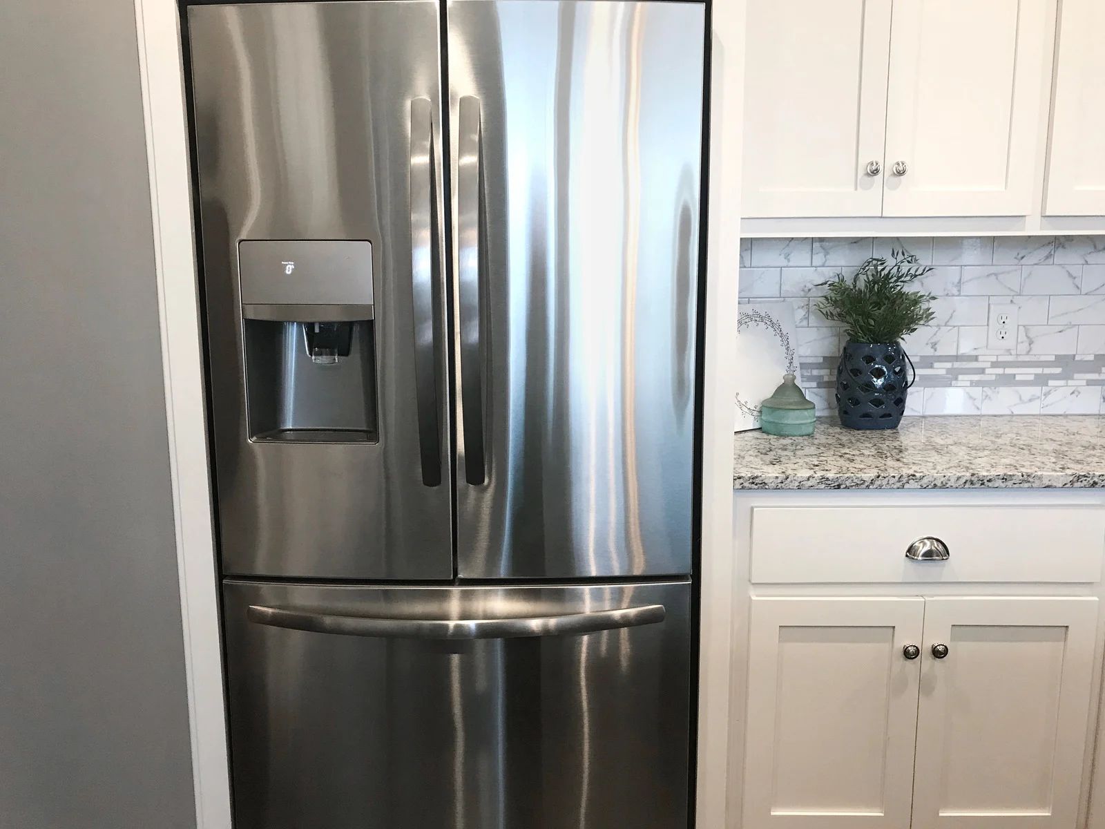 Stainless steel refrigerator in a bright white kitchen with granite countertop and cabinets