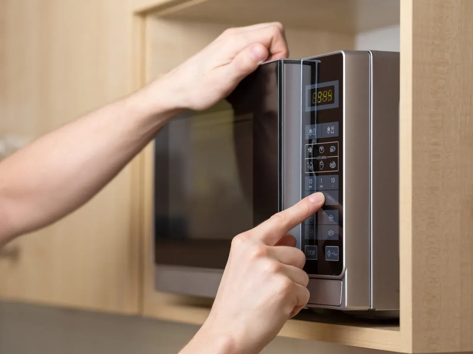 Person presses a button on a microwave, which is built into a light wood cabinet.