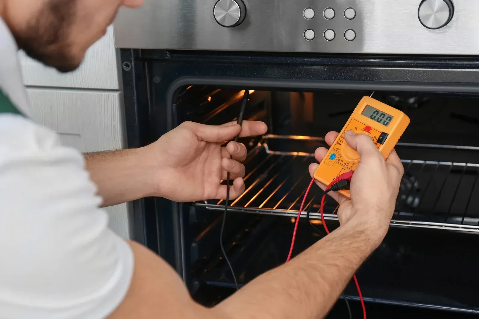A man is fixing an oven with a multimeter.