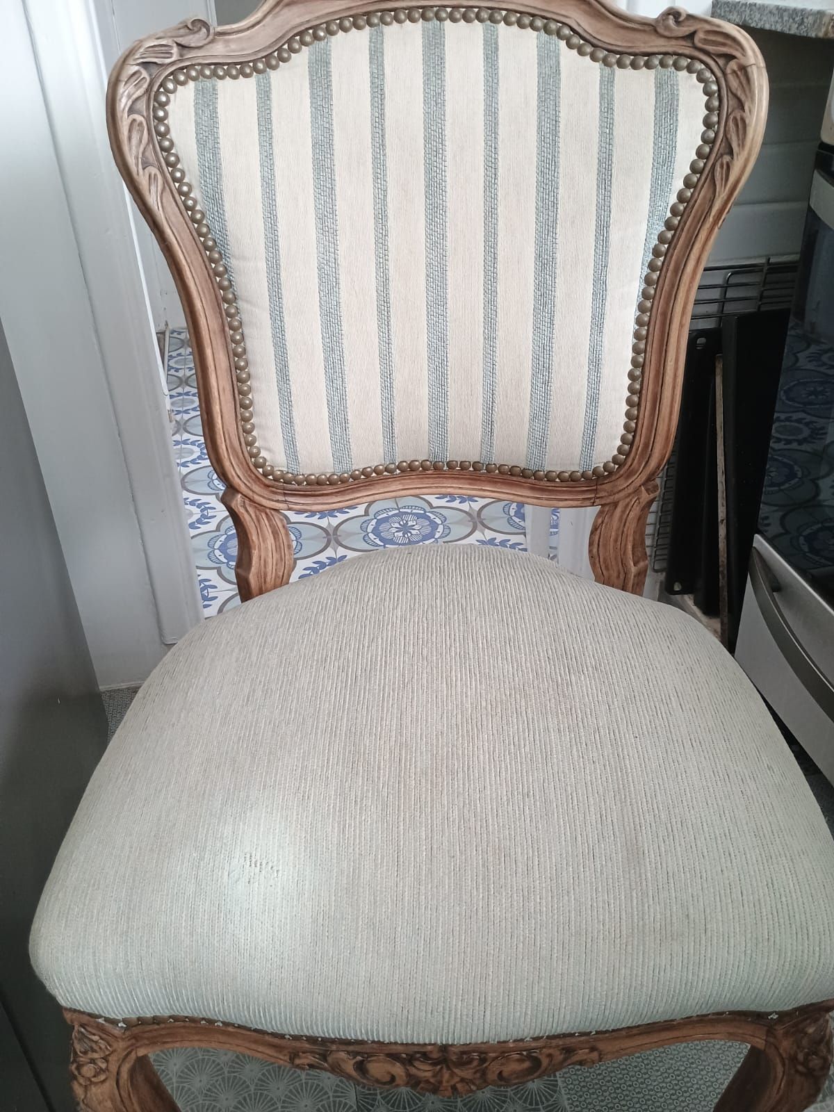 Una silla de madera de estilo antiguo con respaldo de tela a rayas color crema claro y gris