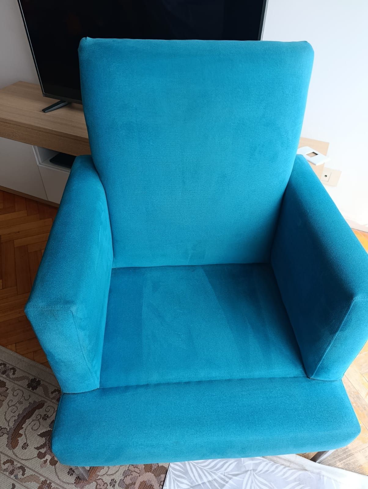 Un sillón de color turquesa brillante tapizado en tela, ubicado en una habitación