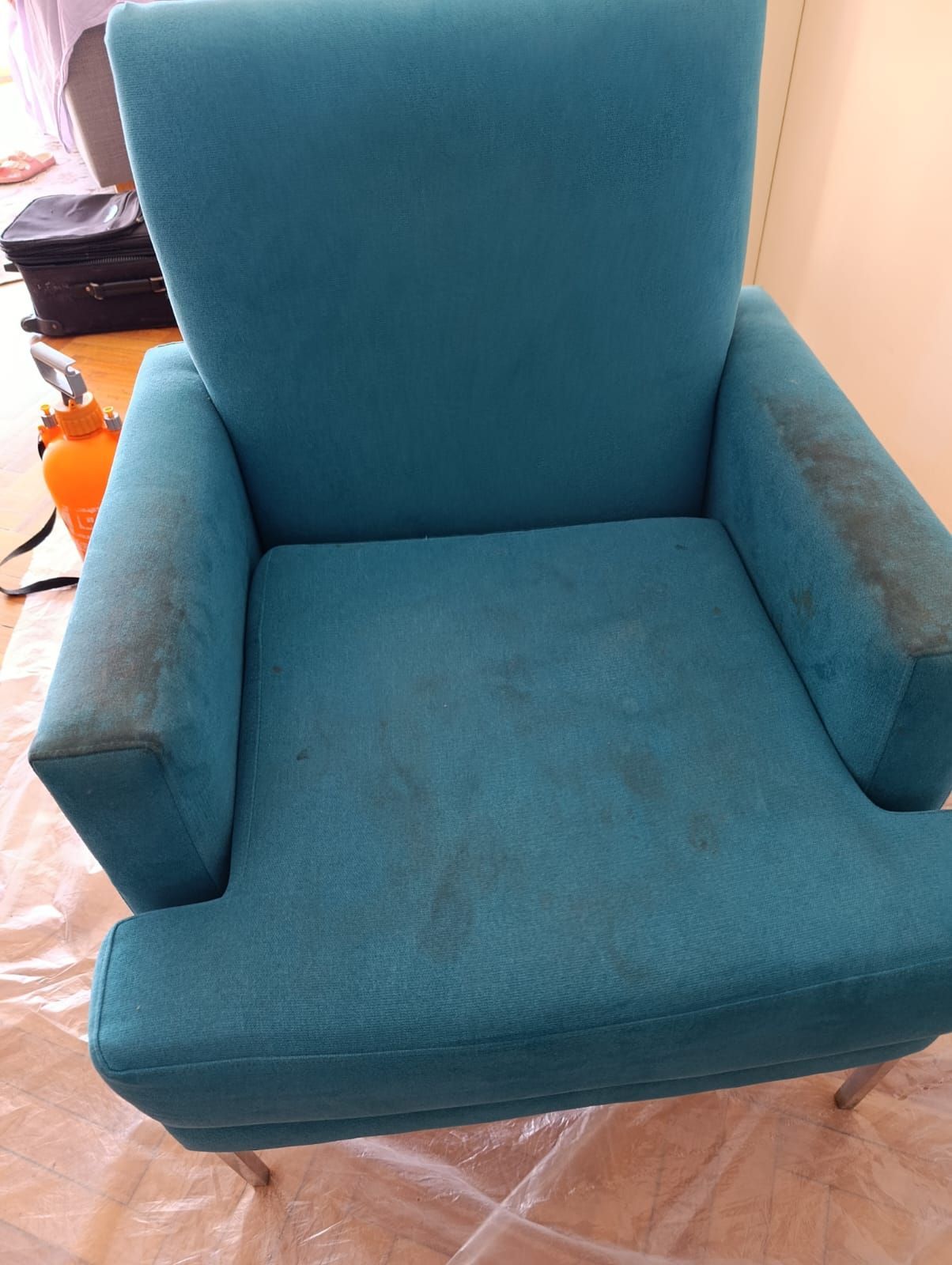Un sillón tapizado en color verde azulado con manchas oscuras visibles en los reposabrazos