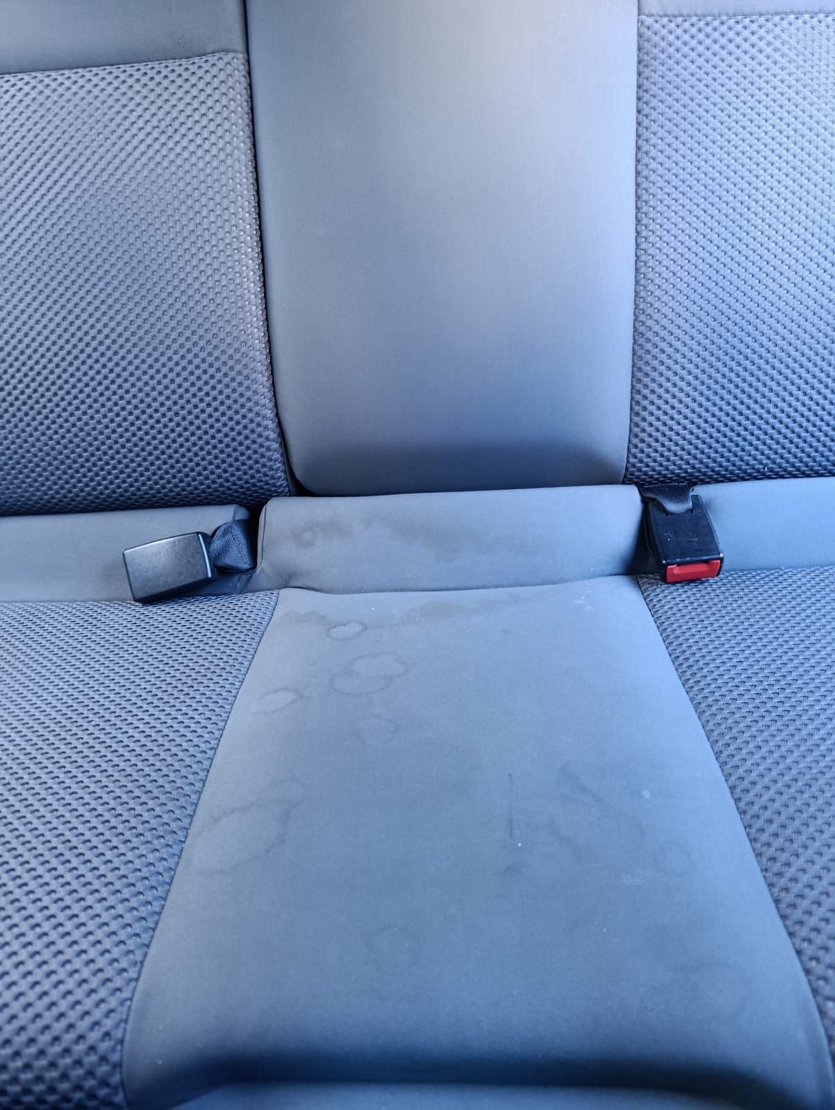 Un sillón tapizado en color verde azulado con manchas oscuras visibles en los reposabrazos y el cojín del asiento