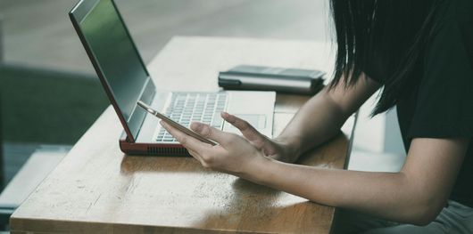 Person using a laptop, holding a pen. They are sitting at a table.