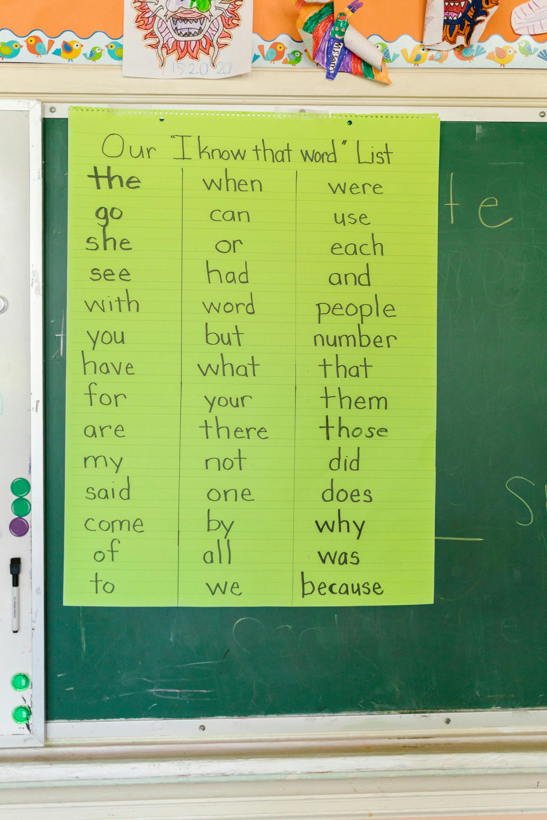 A green sight word list on a chalkboard in a classroom.