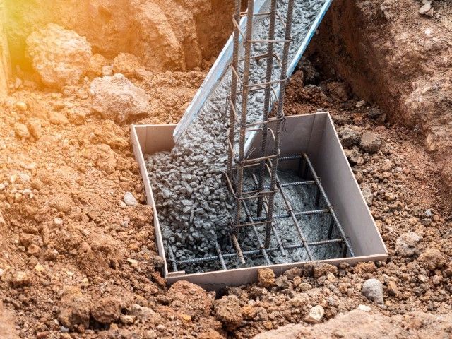 Concrete being poured into a foundation form with rebar. Construction site, outdoors.