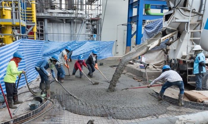 Construction workers spreading wet concrete from a truck using rakes and shovels at a construction site.
