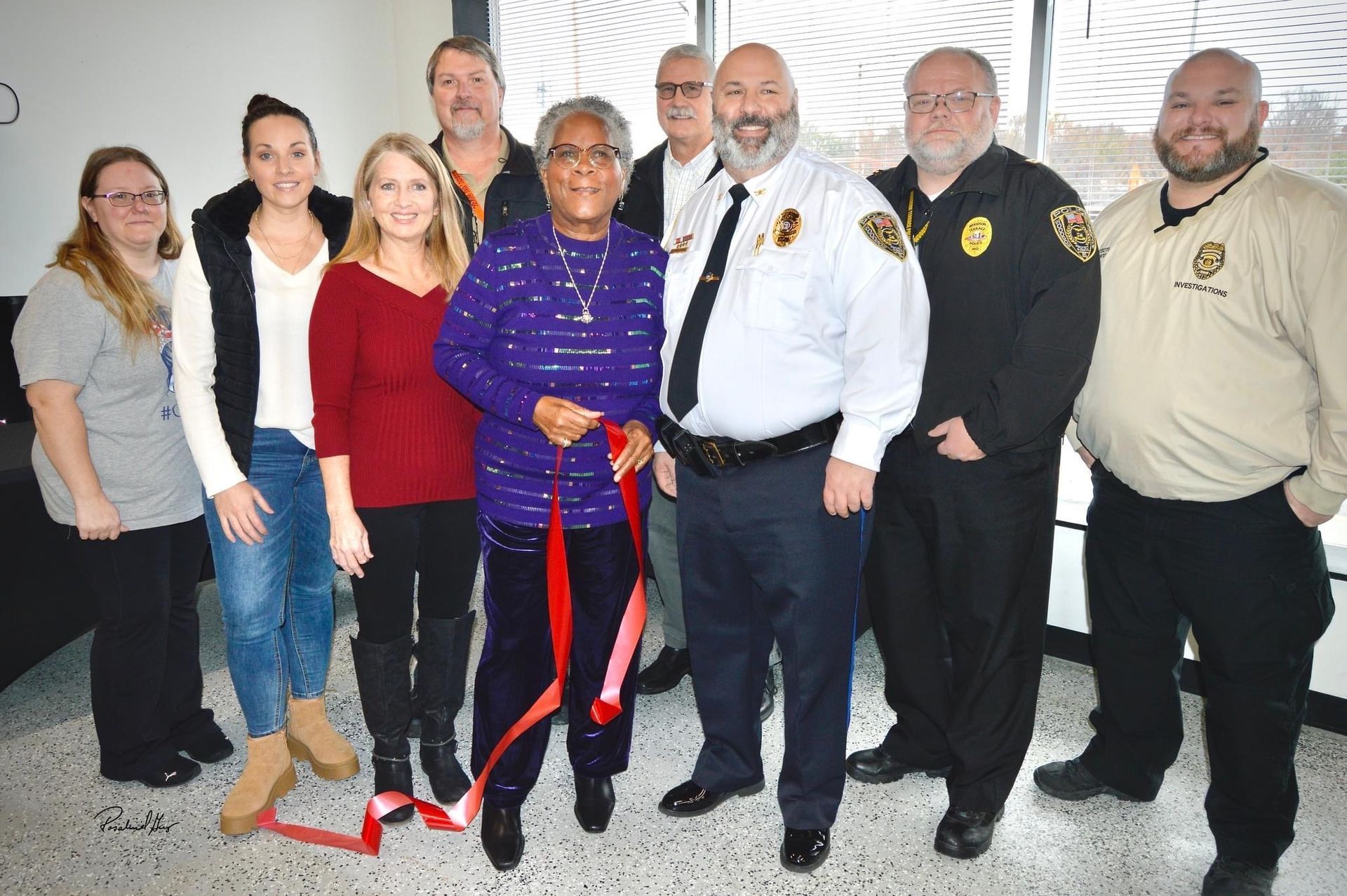 A group of people standing next to each other holding a red ribbon.