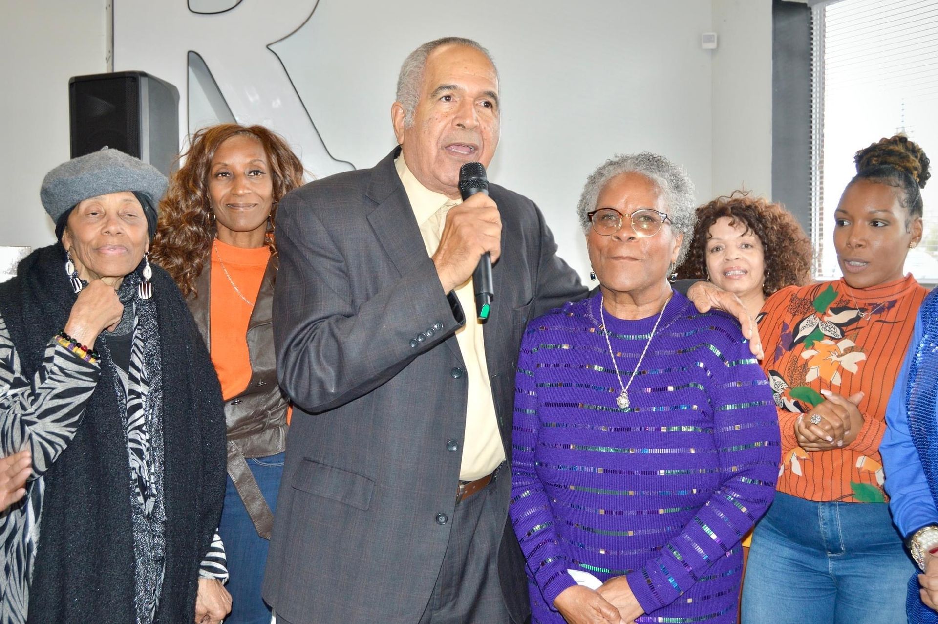 A man in a suit is holding a microphone in front of a group of women.