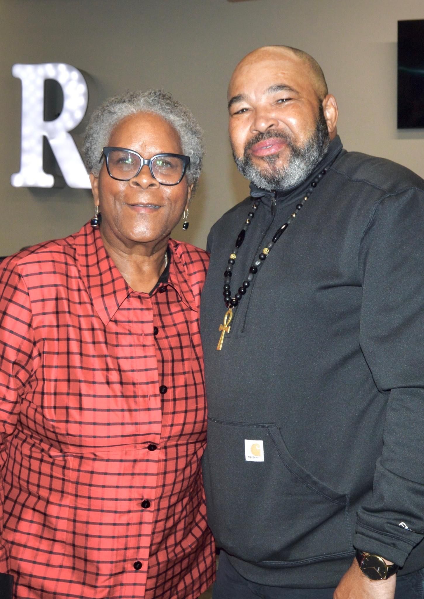 A man and a woman are posing for a picture in front of a sign that says r.
