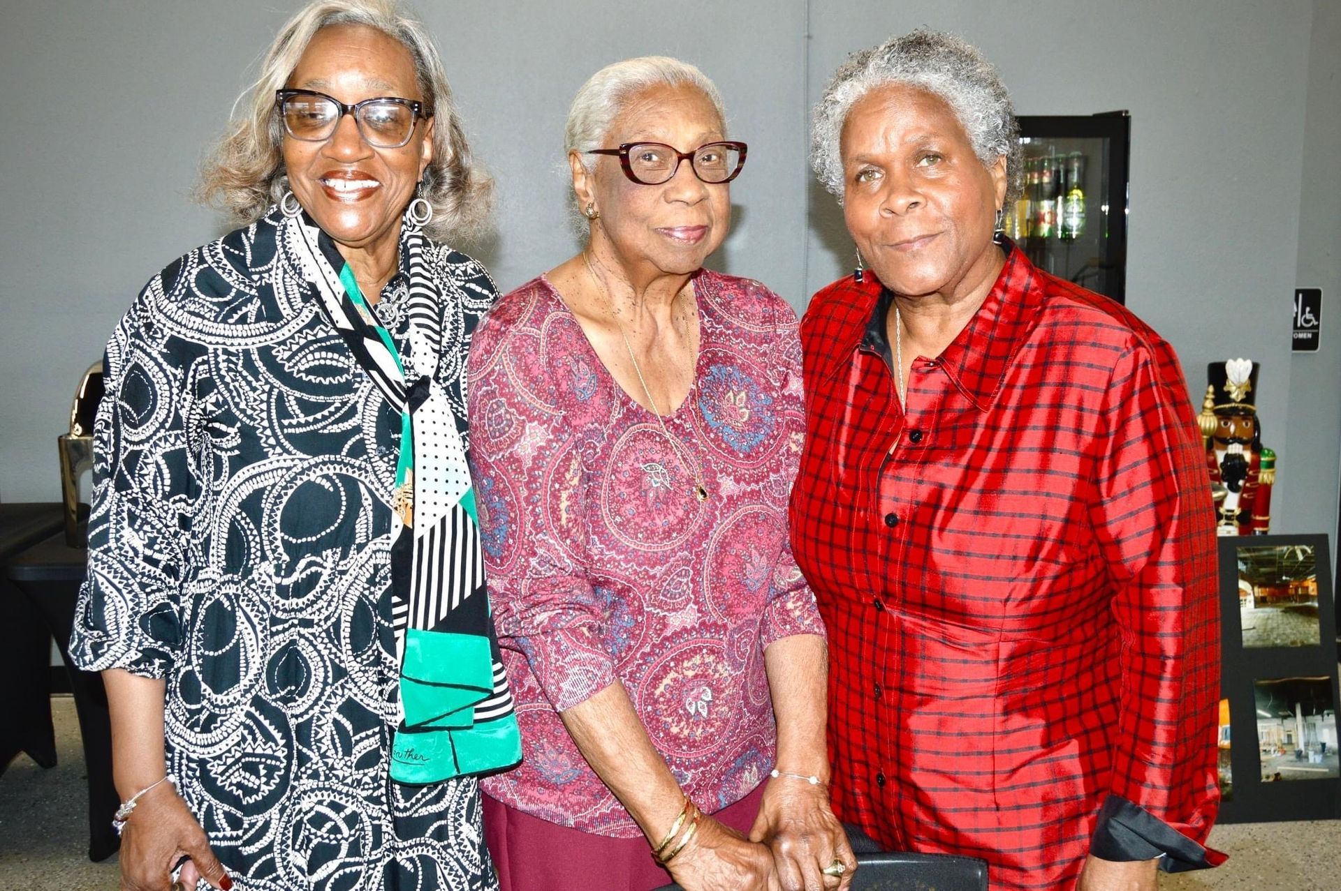 Three older women are posing for a picture together in a living room.