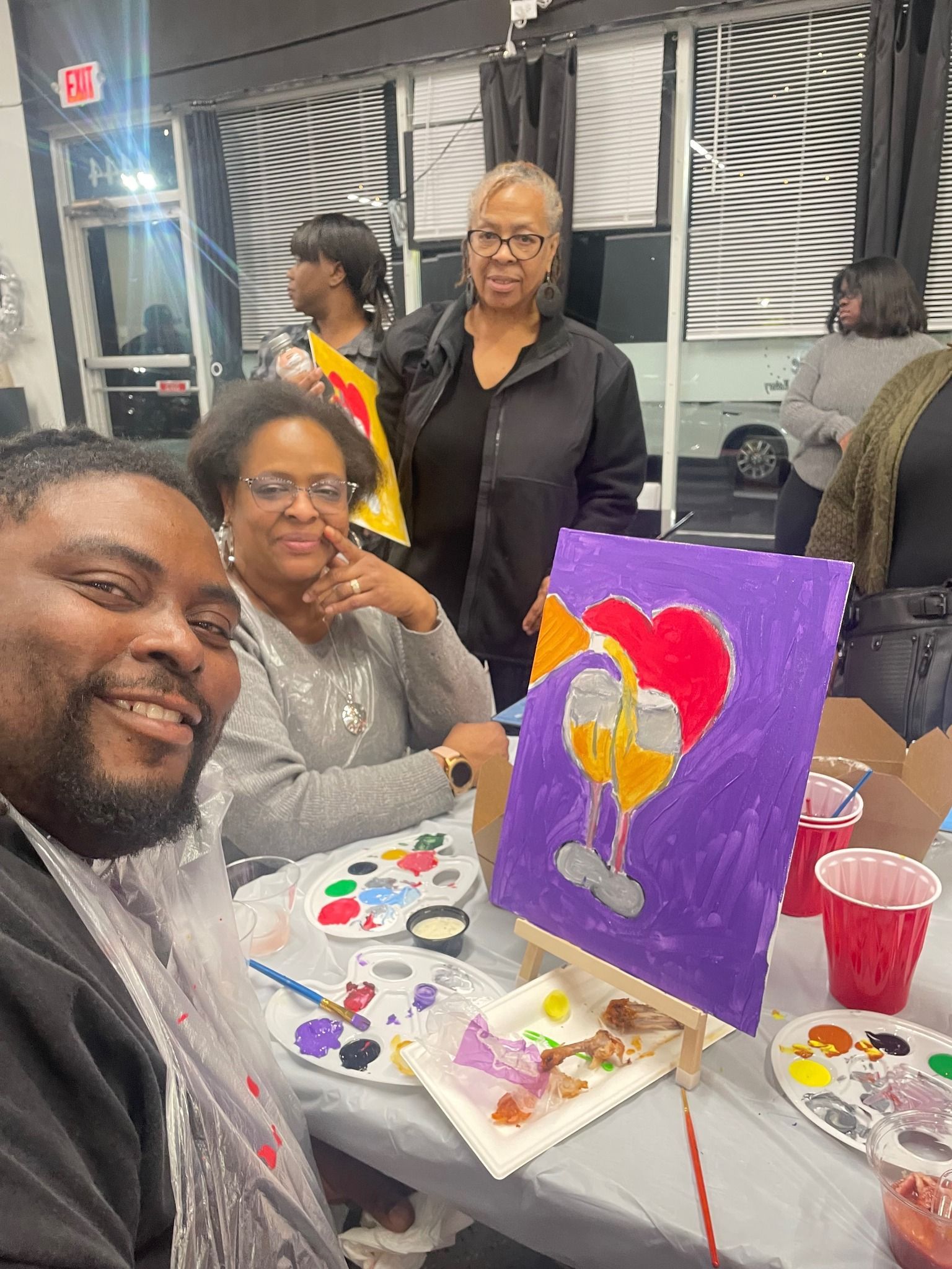 A group of people are sitting at a table with paintings on it.