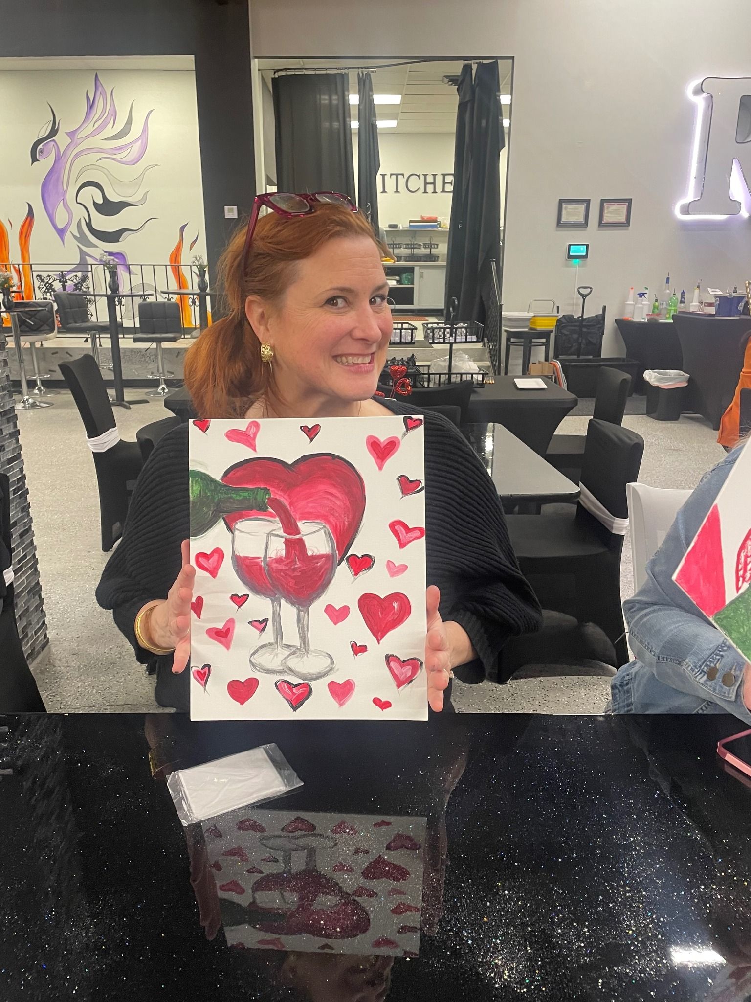 A woman is holding a painting of a heart and a glass of wine.