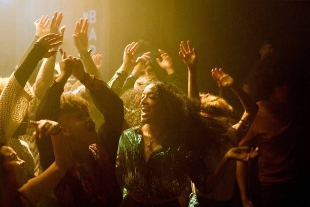 A crowd of people are dancing in a club with their hands in the air.