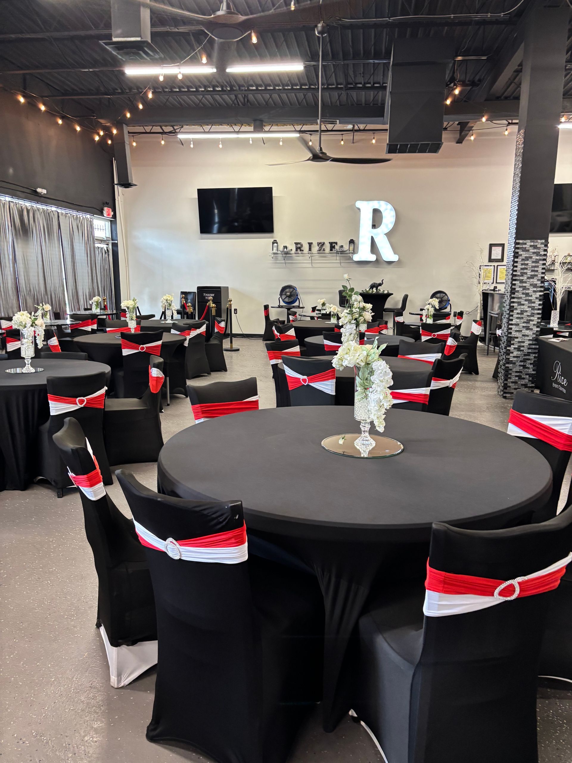A large room with tables and chairs set up for a party with a large letter r on the wall.