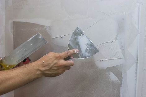 Mano che usa una spatola per raschiare o riparare il cartongesso crepato su una parete bianca