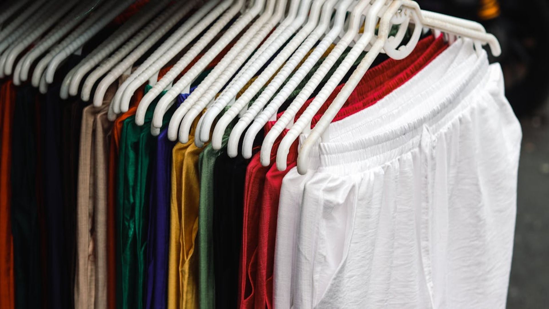 Pantalones coloridos en perchas blancas en una tienda, incluidos blancos, rojos y azules.