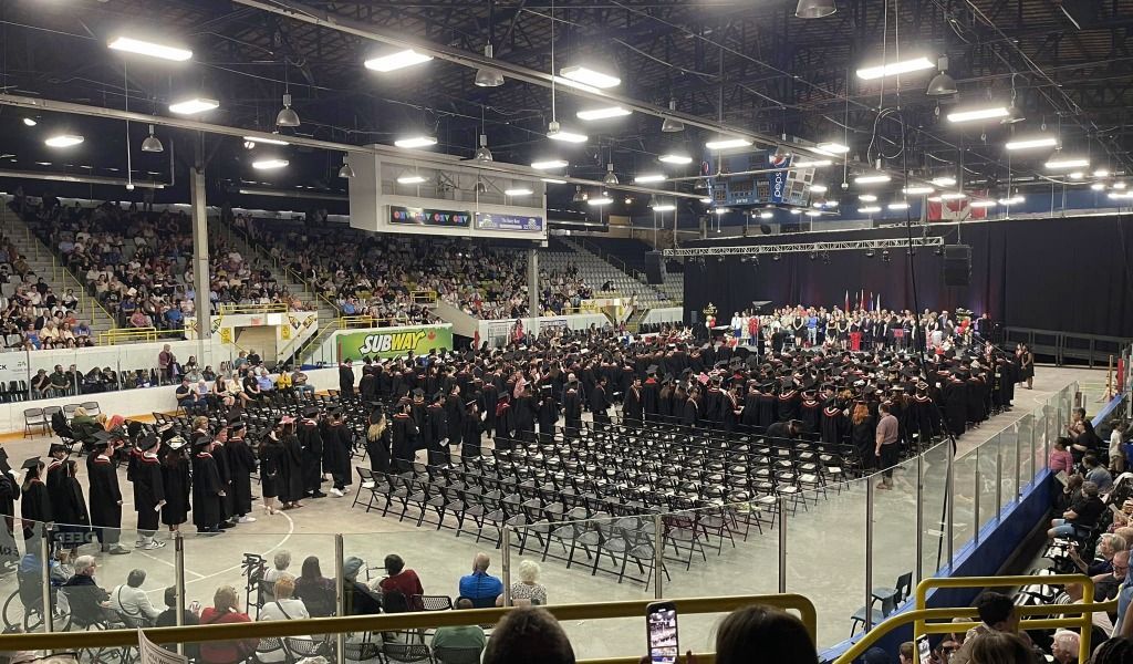 A large group of people are sitting in a stadium watching a graduation ceremony.