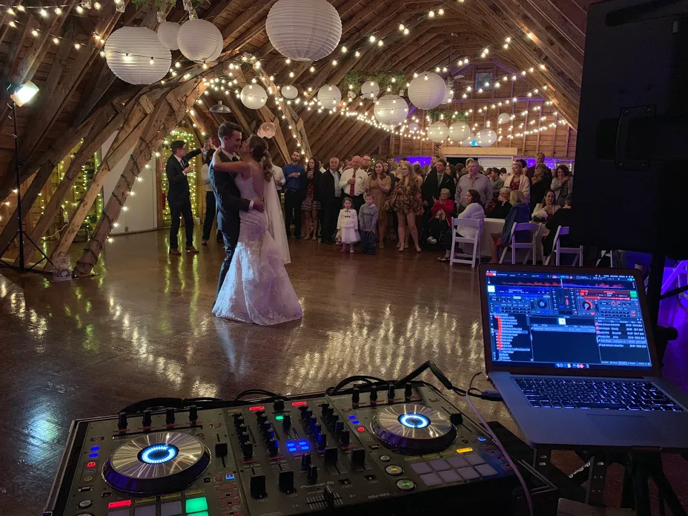 A bride and groom are dancing at their wedding reception in a barn.