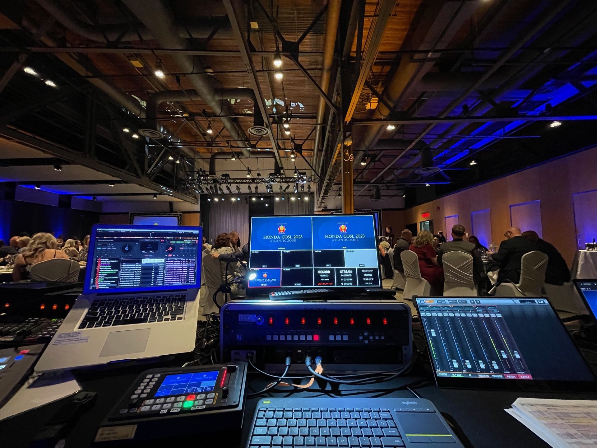 A group of people are sitting at tables in a room with laptops and monitors.