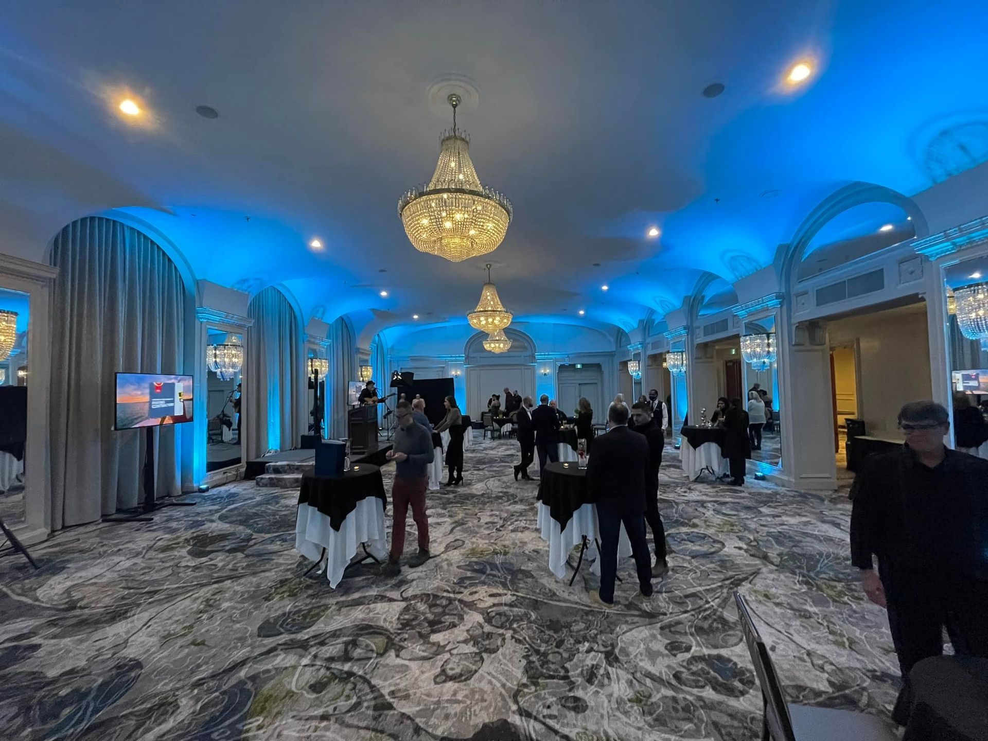 A group of people are standing in a large room with blue lights on the ceiling.