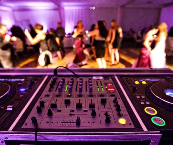 A close up of a dj mixer with people dancing in the background.