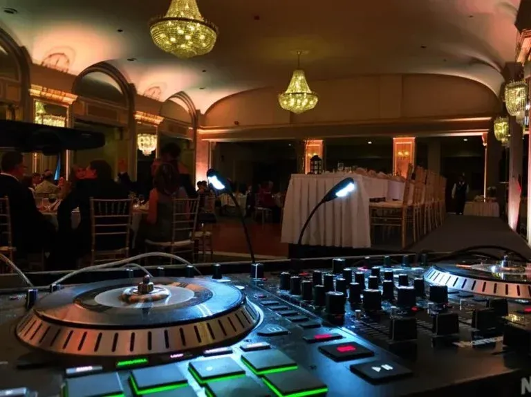 A dj mixer in a large room with people sitting at tables.