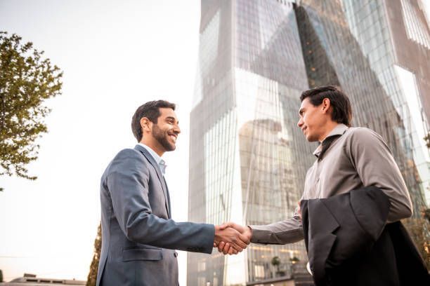 Two men are shaking hands in front of a tall building.