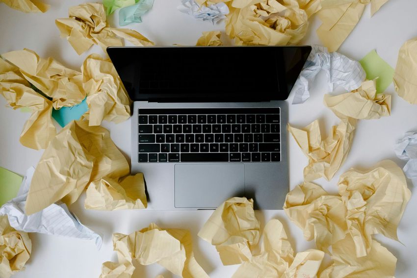 A laptop computer is surrounded by crumpled paper on a table.