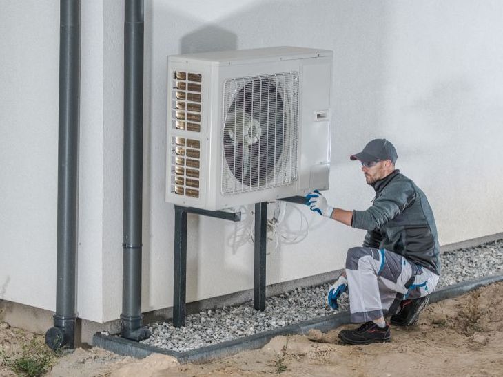 Un homme installe un climatiseur sur le côté d'un bâtiment.